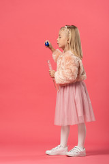 side view of cute kid blowing soap bubbles on pink background