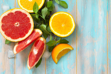 Ingredients for cooking a refreshing drink. Grapefruit, orange, ice and basil on a wooden table. Top view on a flat background. Copy space.