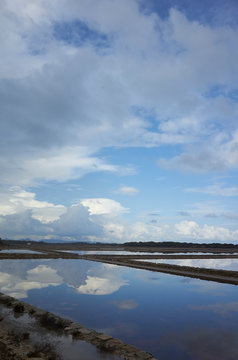 Parcelas de salinas separadas por muros de piedra reflejando un cielo azul con nubes