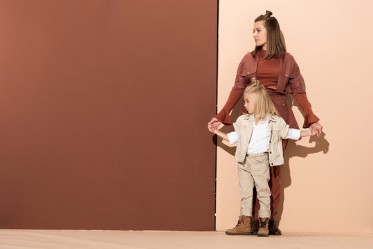 Cute Daughter And Attractive Mother Holding Hands On Beige And Brown Background