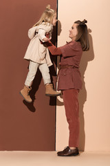 side view of mother holding smiling daughter on beige and brown background