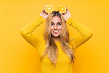 Young blonde woman holding an orange over yellow background