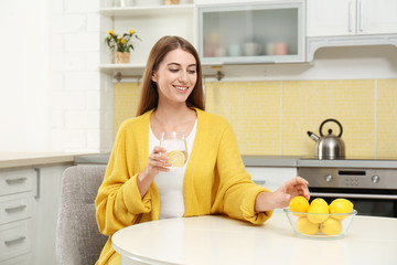 Young woman with glass of lemon water in kitchen