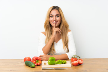Young blonde woman with vegetables in a table doing silence gesture