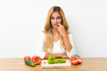 Young blonde woman with vegetables in a table nervous and scared