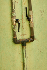 Old water pipes with flaking paint on a green wall in Sudan