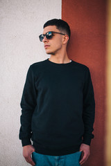 Obraz premium City portrait of handsome hipster guy with beard wearing black blank hoody or sweatshirt with space for your logo or design. Mockup for print