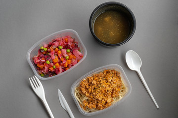 Pasta with minced meat and onion in navy-style and a jar of vinaigrette on a gray background. Food from delivery. Nearby are disposable cutlery.
