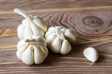 Three heads of raw garlic and one clove on a brown wooden table. Spicy cooking ingredient. Vitamin healthy food. Vegetables and vegetarian.