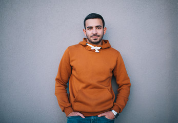 City portrait of handsome hipster guy with beard wearing brown blank hoodie or hoody with space for your logo or design. Mockup for print