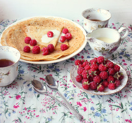 cup of tea, pancake with cream and raspberries on the table