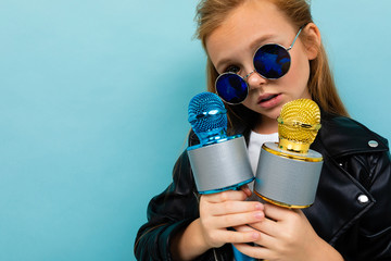 portrait european girl in sunglasses with two microphones in hands on a light blue background