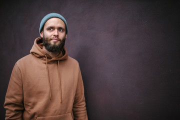 City portrait of handsome hipster man with beard wearing brown blank hoodie or hoody with space for your logo or design. Mockup for print
