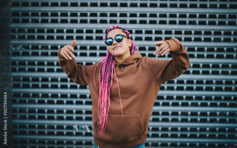 Wall mural City portrait of handsome hipster girl with colored afro braids wearing brown blank hoodie or hoody with space for your logo or design. Mockup for print - Wall murals