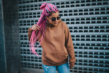 City portrait of handsome hipster girl with colored afro braids wearing brown blank hoodie or hoody...