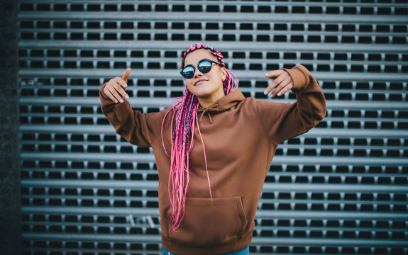 City Portrait Of Handsome Hipster Girl With Colored Afro Braids Wearing Brown Blank Hoodie Or Hoody With Space For Your Logo Or Design. Mockup For Print