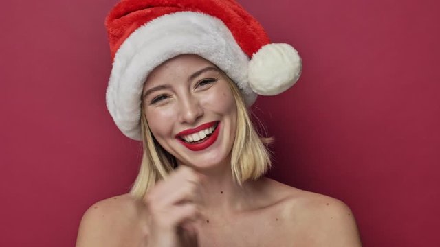 Happy cheerful smiling young woman with red lipstick wearing santa clause hat is appearing isolated over red background