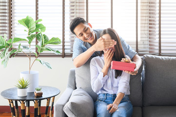 Asian man giving a gift box present to surprise his girlfriend at home