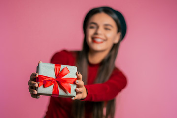 Fototapeta premium Pretty woman gives gift and hands it to the camera. She is happy, smiling. Girl on pink background. Positive holiday shot. 