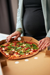 Cutout picture of caucasian pregnant business woman in forties and dressed in suit standing in office and having pizza for lunch.