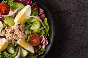 Salad with tuna, egg and vegetables on black background top view copy space	