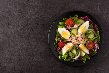 Salad with tuna, egg and vegetables on black background top view copy space	
