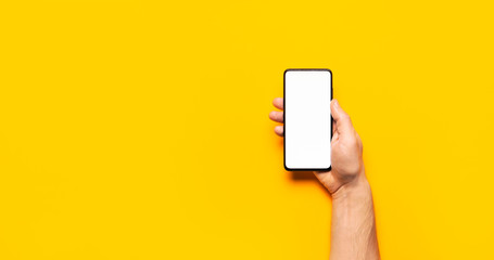 Male hands hold a modern black smartphone with white blank screen on yellow background. Modern...