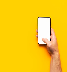 Fototapeta na wymiar Male hands hold a modern black smartphone with white blank screen on yellow background. Modern technology, phone, gadget in hands, touch screen, template for your design. Mockup
