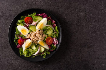 Salad with tuna, egg and vegetables on black background top view copy space	