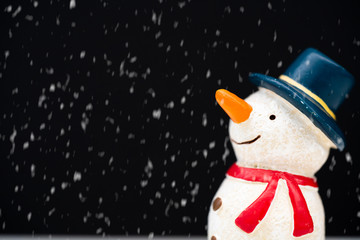 Happy smiley snowman wear blue hat and carrot nose standing with snowflakes in winter christmas season.Black background.Christmas scenes.