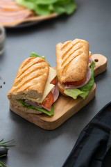 Sandwich with baguette bread, ham, lettuce, tomatoe over dark background. Breakfast or fast food.