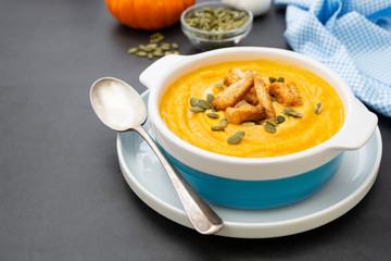Creamy carrot soup, autumn foods. Spicy, roasted vegetable soup in bowl. Dark background.