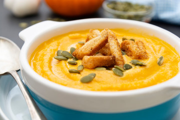 Creamy carrot soup, autumn foods. Spicy, roasted vegetable soup in bowl. Dark background.