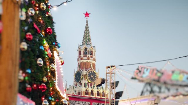Beautiful view to the Moscow Kremlin Clock on Spasskaya Tower through the colorful New Year garlands and decorated Christmas trees on Red Square on winter evening.