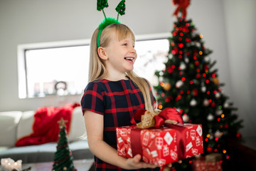 Happy girl in christmas outfit holding red present