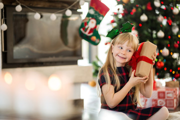Young happy girl holding christmas gift wondering what's inside