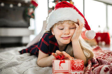 Happy girl in santa hat lying on floor with red present