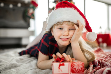 Cheerful girl in santa hat lying on floor with present
