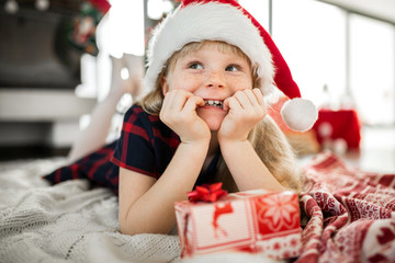 Excited girl in santa hat lying on floor thinking