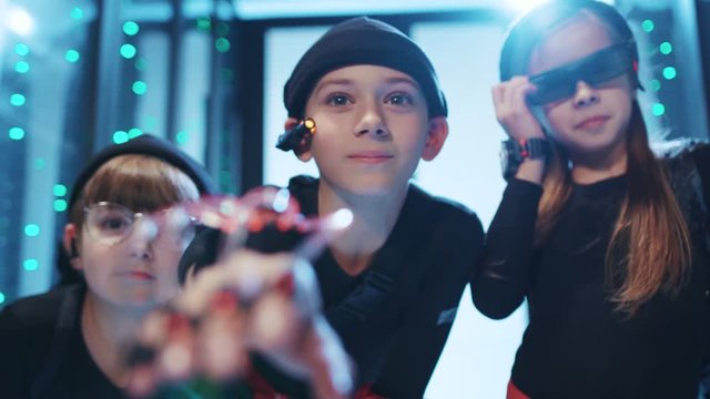 Team of young curious hackers sneaking into server room of data center. Spy kid wearing robotic exoskeleton hand controlling virtual computer interface hacking database supercomputer.
