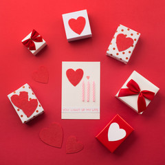 Handmade wrapped gift boxes, red hearts and candles, red background