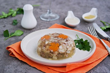 Cold appetizer, portioned meat jelly of pork, beef and chicken on a white clay plate on a gray concrete background. Holiday appetizer for New Year. Russian cuisine. Selective focus.