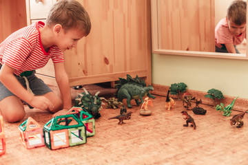 Happy boy plays with toy dinosaurs and a magnetic constructor in a children room sitting on a cork...