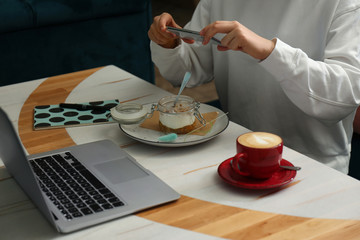 Blogger taking picture of dessert at table in cafe, closeup