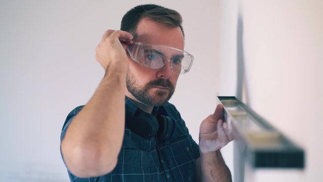 Dolly cam: bearded builder in protective goggles stressed out of troubles with wrong wall angle in light empty room closeup