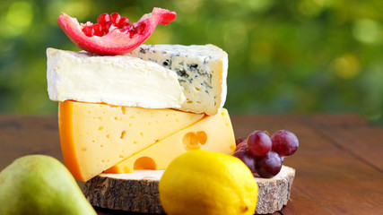 Camembert, brie, hard cheese and grapes on wooden stand. Pieces of different cheeses, pear and...