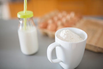 Mug with flour and bottle of milk on kitchen table