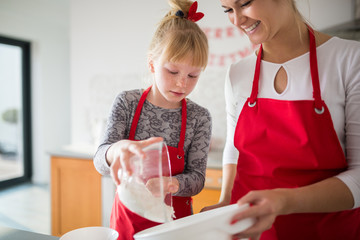 Young girl helping mom pouring flour to bowl