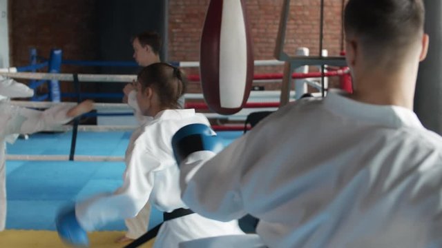 Back view of four sparring partners wearing white kimonos and boxing gloves practicing kicks and punches in gym