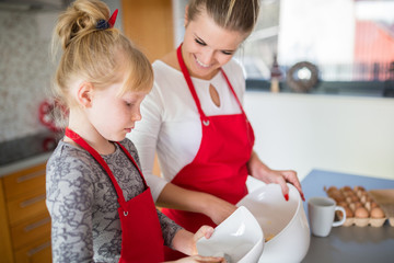Young girl focused on helping her mom making dough